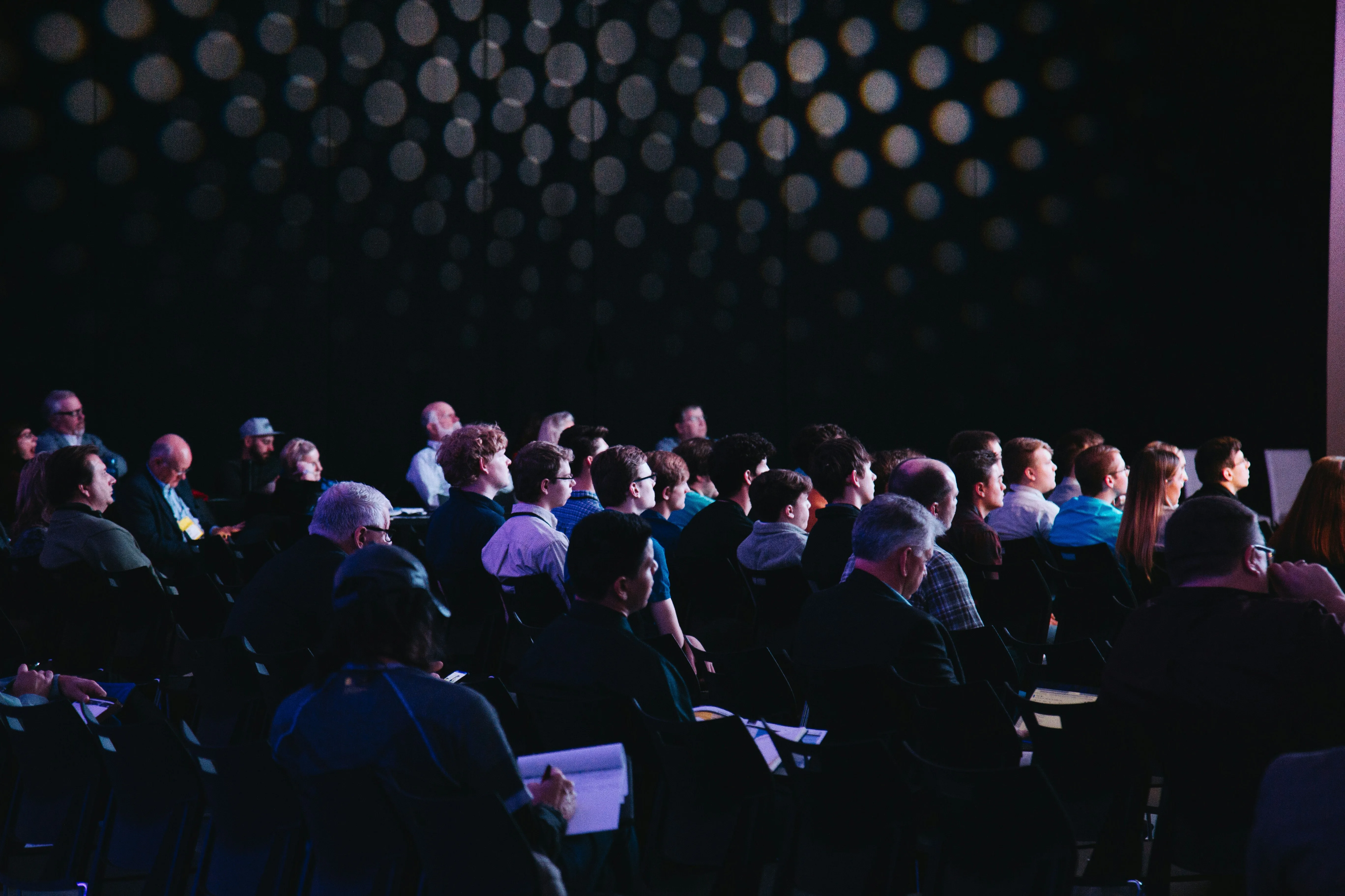 A photo of a conference with lots of people looking at the speaker